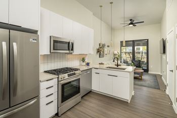A modern kitchen with gas stove, stainless steel appliances, quartz counters and white cabinetry.